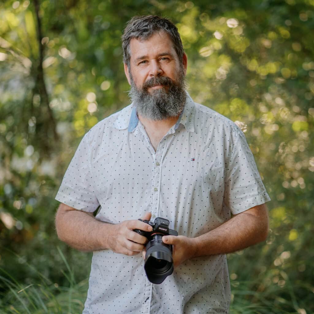 Photo of Tony holding a camera and looking at camera.