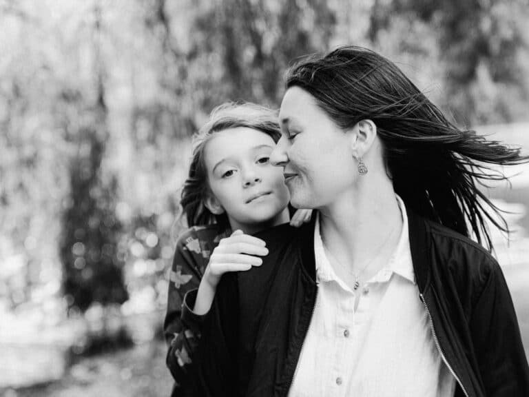 Kate looking back at Rey who is leaning on her shoulder looking towards camera during a family session at Lake Te Koo Utu in Cambridge