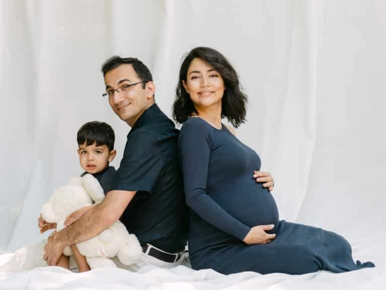 Tina and Pouya back to back while Neil sits on dads legs with teddy during a maternity session at home