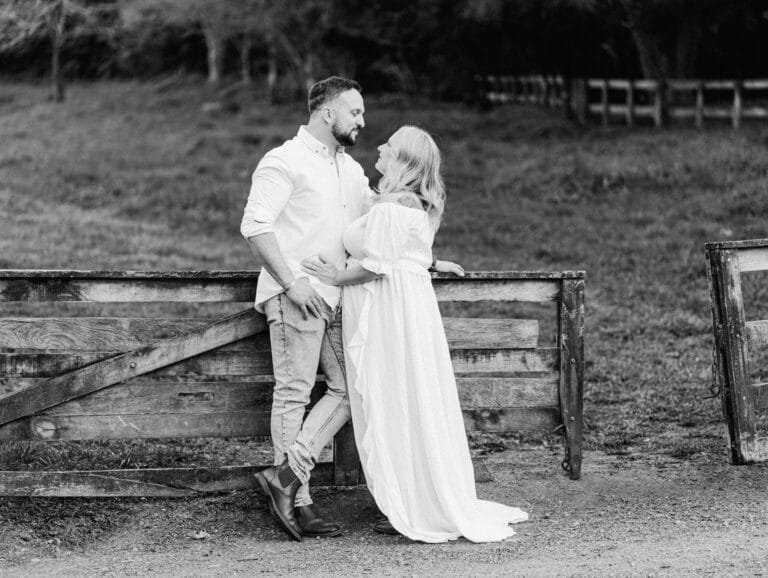 Melissa and Mike leaning on wooden fence with tummies together during a maternity session at Taitua Arboretum