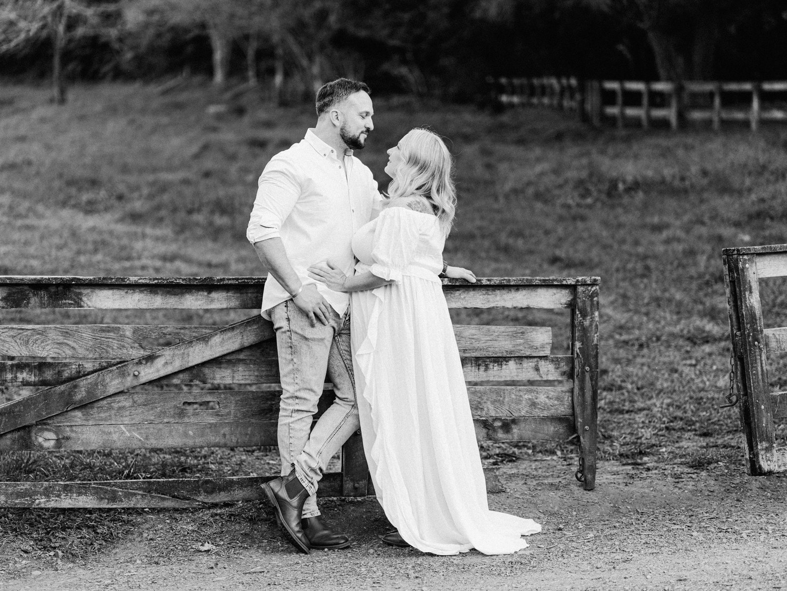 Melissa and Mike leaning on wooden fence with tummies together during a maternity session at Taitua Arboretum