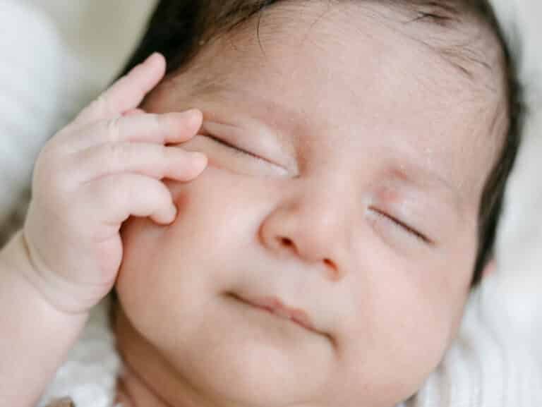 baby face smiling in sleep with hand on side of face during a newborn session at home in Hamilton