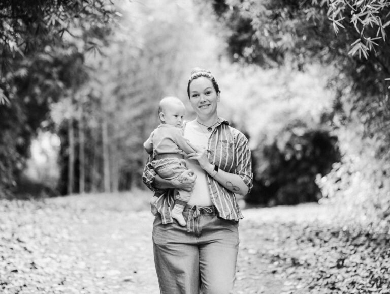 Tee looking towards camera while holding little Jack during a family session at Taitua Arboretum