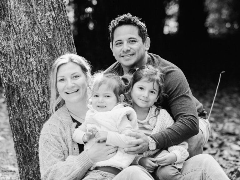 dad, mum and two daughters looking at camera while sitting together during a family session at Taitua Arboretum